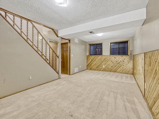 finished basement featuring stairway, wooden walls, visible vents, carpet floors, and a textured ceiling