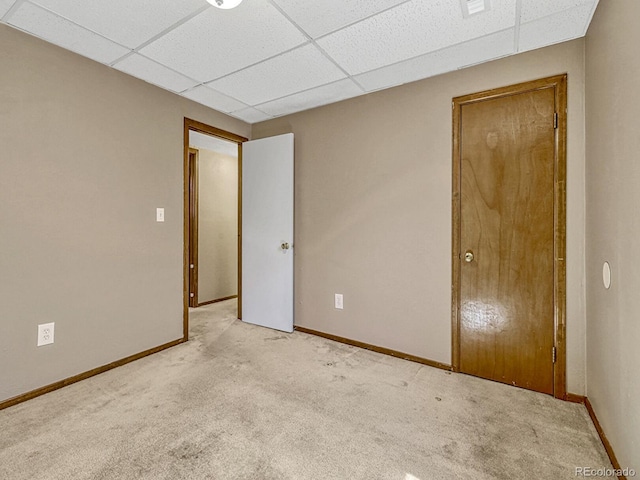 unfurnished bedroom with a paneled ceiling, baseboards, and light carpet