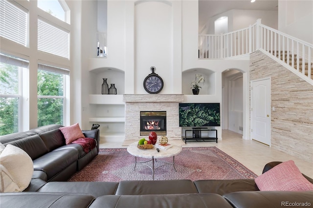 tiled living room featuring built in shelves, a high ceiling, and a stone fireplace