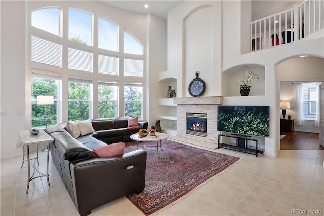 living room featuring a towering ceiling, plenty of natural light, light tile patterned floors, and a stone fireplace