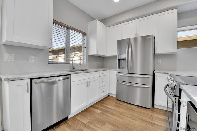 kitchen with light wood-style flooring, a sink, stainless steel appliances, white cabinets, and light stone countertops