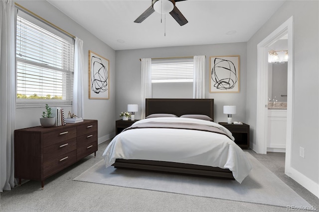 bedroom with light carpet, a ceiling fan, ensuite bath, and baseboards