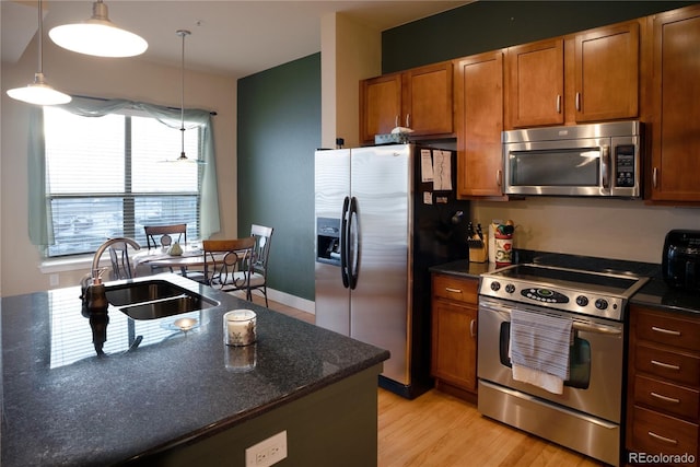 kitchen with sink, light wood-type flooring, hanging light fixtures, and appliances with stainless steel finishes