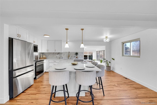 kitchen with pendant lighting, backsplash, white cabinets, sink, and stainless steel appliances