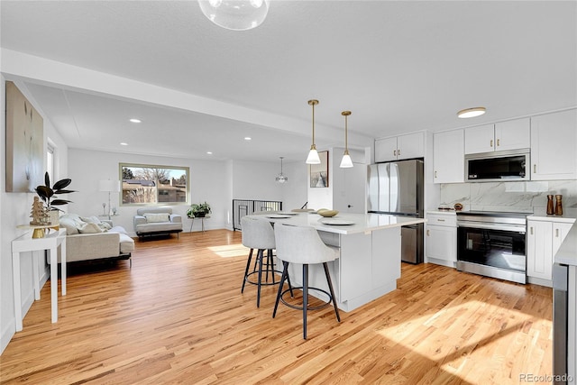 kitchen with a kitchen bar, appliances with stainless steel finishes, pendant lighting, a center island, and white cabinetry