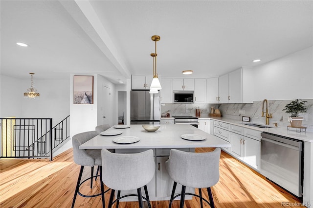 kitchen with sink, hanging light fixtures, decorative backsplash, white cabinetry, and stainless steel appliances