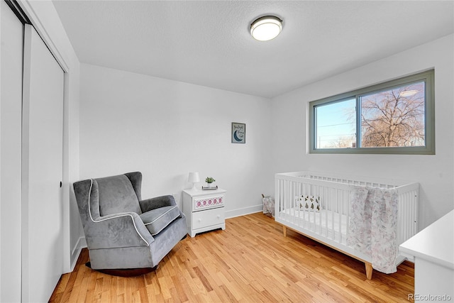 bedroom with a textured ceiling, a closet, a crib, and light wood-type flooring