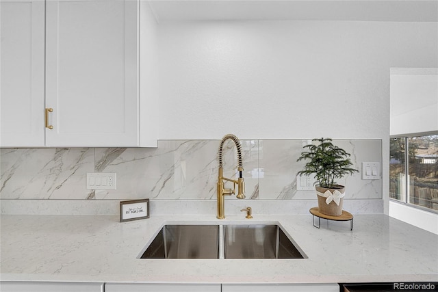 room details with white cabinetry, sink, light stone countertops, and tasteful backsplash