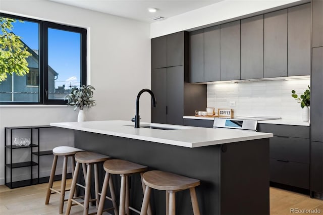 kitchen with gray cabinetry, a kitchen breakfast bar, light wood-type flooring, and sink