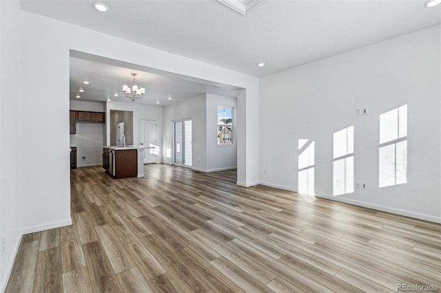 unfurnished living room with light wood finished floors, recessed lighting, a sink, a chandelier, and baseboards