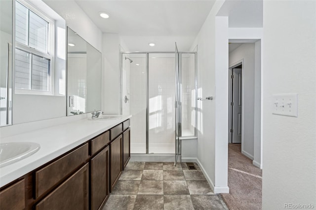 bathroom with double vanity, a stall shower, baseboards, and a sink