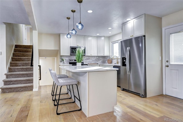 kitchen featuring white cabinetry, hanging light fixtures, stainless steel appliances, and light hardwood / wood-style flooring