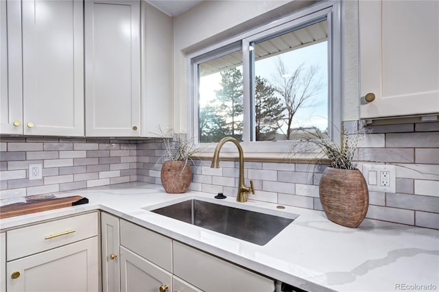 kitchen featuring backsplash, light stone counters, white cabinets, and sink