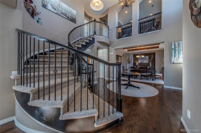 staircase with wood-type flooring, a towering ceiling, and an inviting chandelier