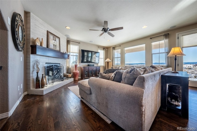 living room with a fireplace, a textured ceiling, dark hardwood / wood-style flooring, and ceiling fan