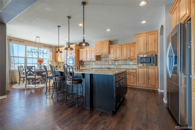 kitchen with pendant lighting, decorative backsplash, an island with sink, appliances with stainless steel finishes, and light stone counters