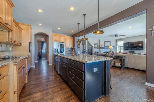 kitchen with sink, stainless steel appliances, backsplash, decorative light fixtures, and a kitchen island with sink