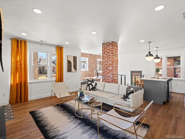 living room featuring dark wood-type flooring, brick wall, and a healthy amount of sunlight