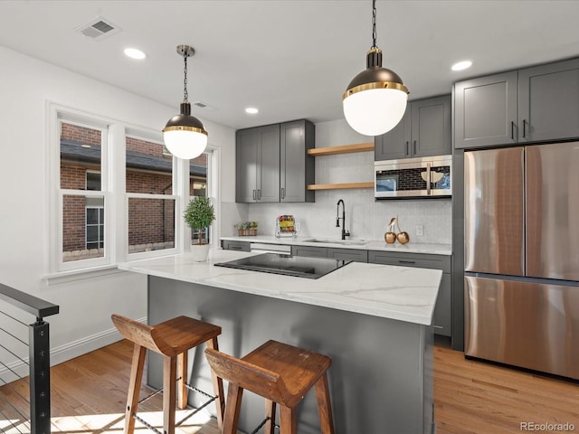 kitchen with gray cabinets, sink, stainless steel appliances, light stone countertops, and light wood-type flooring