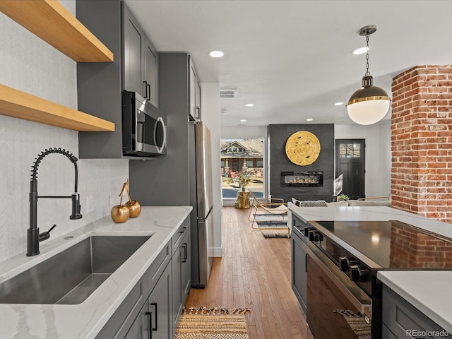 kitchen with sink, a large fireplace, gray cabinets, stainless steel appliances, and light stone countertops