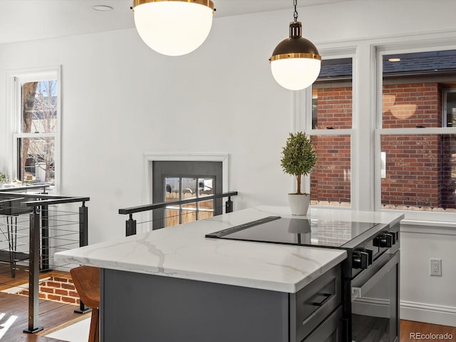 kitchen with black electric range oven, hardwood / wood-style flooring, gray cabinets, pendant lighting, and light stone countertops