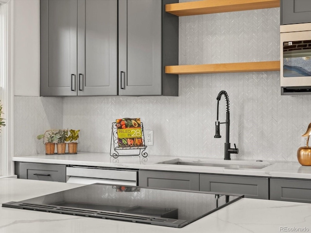 kitchen featuring gray cabinets, tasteful backsplash, light stone countertops, and sink