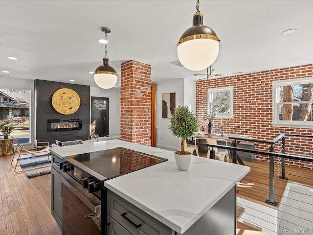 kitchen featuring pendant lighting, light hardwood / wood-style flooring, light stone counters, range with electric stovetop, and a large fireplace