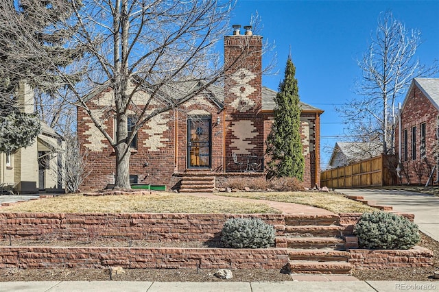 tudor home featuring fence, brick siding, and a chimney