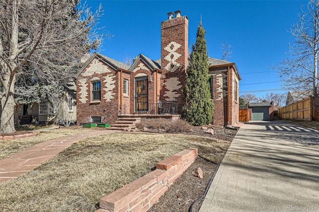 english style home featuring brick siding, an outdoor structure, a chimney, and fence