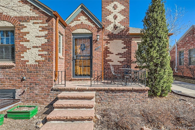 doorway to property featuring brick siding, a chimney, and a shingled roof