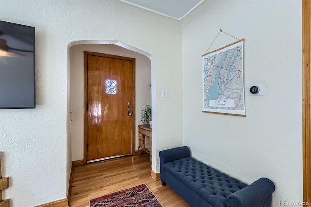 entrance foyer with wood finished floors, arched walkways, a textured wall, and baseboards