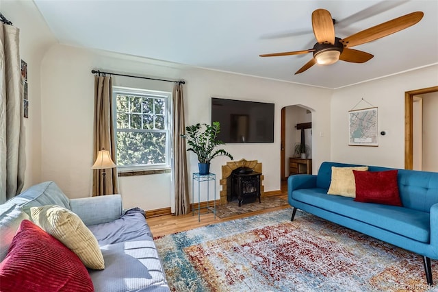 living area featuring baseboards, a wood stove, wood finished floors, arched walkways, and a ceiling fan