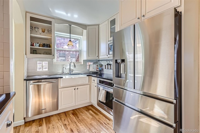 kitchen with light wood-type flooring, tasteful backsplash, dark countertops, stainless steel appliances, and glass insert cabinets