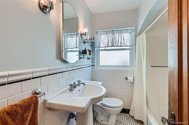 bathroom featuring shower / bath combo with shower curtain, toilet, a sink, tile walls, and wainscoting