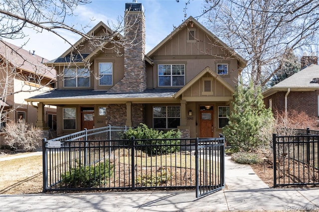 view of front of home with a shingled roof, a porch, a fenced front yard, and a chimney