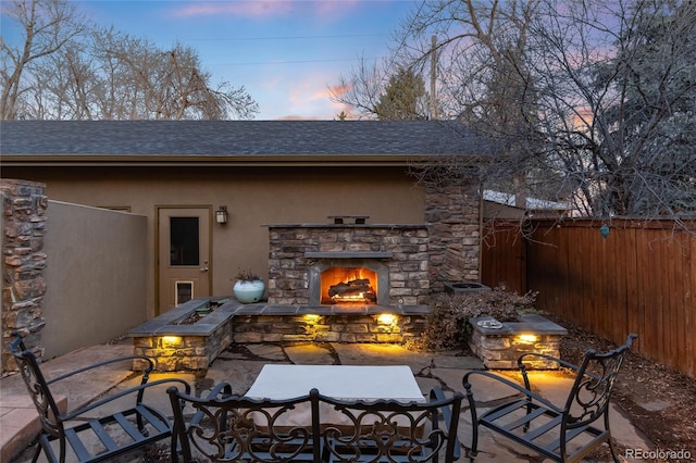 patio terrace at dusk featuring an outdoor stone fireplace and fence