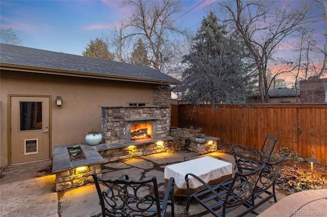 patio terrace at dusk with a fenced backyard and an outdoor stone fireplace