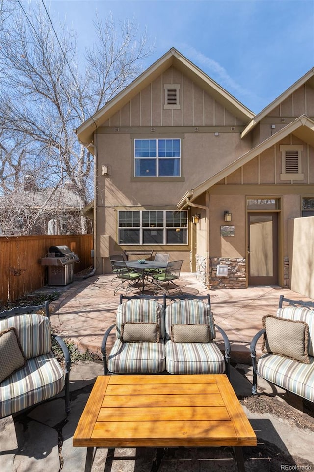 rear view of house with stucco siding, a patio, fence, board and batten siding, and outdoor dining area