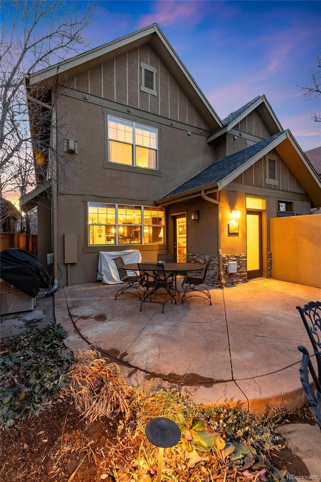 back of property at dusk with stucco siding, a patio, and board and batten siding