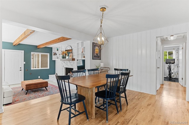 dining room featuring light wood-style flooring, a stone fireplace, and beam ceiling