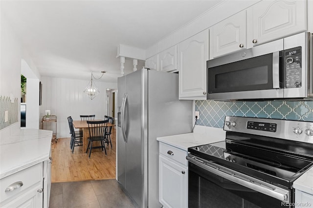 kitchen with appliances with stainless steel finishes, white cabinetry, tasteful backsplash, light stone counters, and dark tile patterned floors