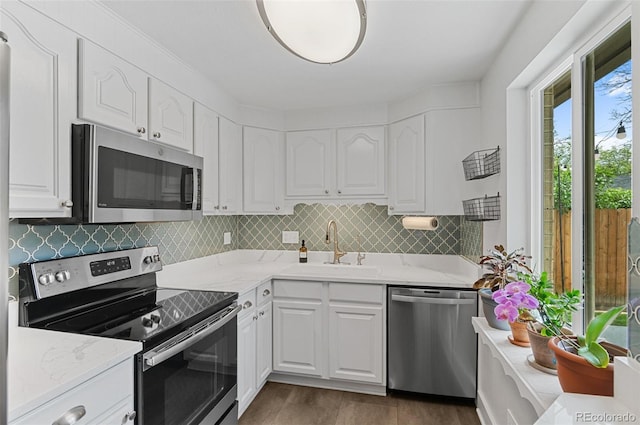 kitchen featuring stainless steel appliances, a sink, white cabinetry, backsplash, and light stone counters