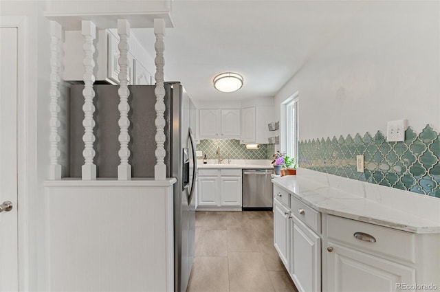 kitchen with stainless steel appliances, white cabinets, tasteful backsplash, a sink, and light stone counters