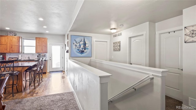 1086 Johnson St, Wiggins, CO 80654 - corridor with an upstairs landing, light wood finished floors, recessed lighting, a sink, and light colored carpet