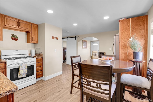 724 County Road 37, Brighton, CO 80603 - kitchen with white range with gas stovetop, stainless steel fridge, arched walkways, a barn door, and brown cabinetry
