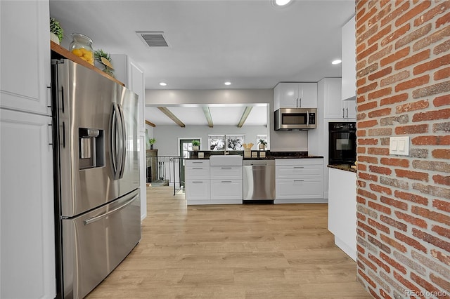 kitchen with stainless steel appliances, light hardwood / wood-style floors, white cabinetry, and brick wall