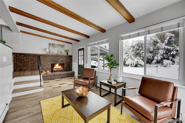 living room featuring a brick fireplace, a baseboard radiator, light hardwood / wood-style floors, and vaulted ceiling with beams