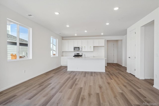 kitchen with appliances with stainless steel finishes, a center island with sink, white cabinetry, and light hardwood / wood-style flooring