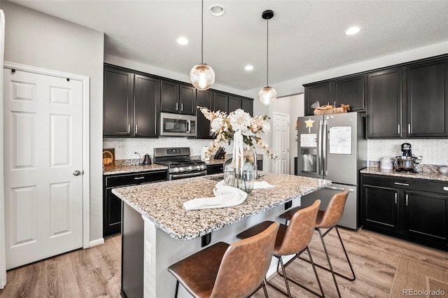 kitchen with decorative light fixtures, stainless steel appliances, light hardwood / wood-style flooring, and an island with sink