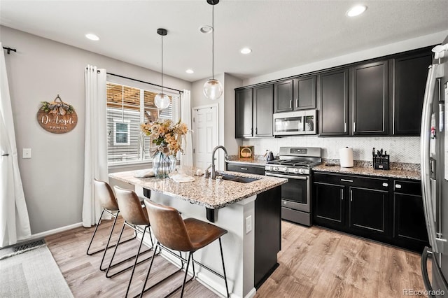 kitchen featuring sink, stainless steel appliances, an island with sink, decorative light fixtures, and a breakfast bar